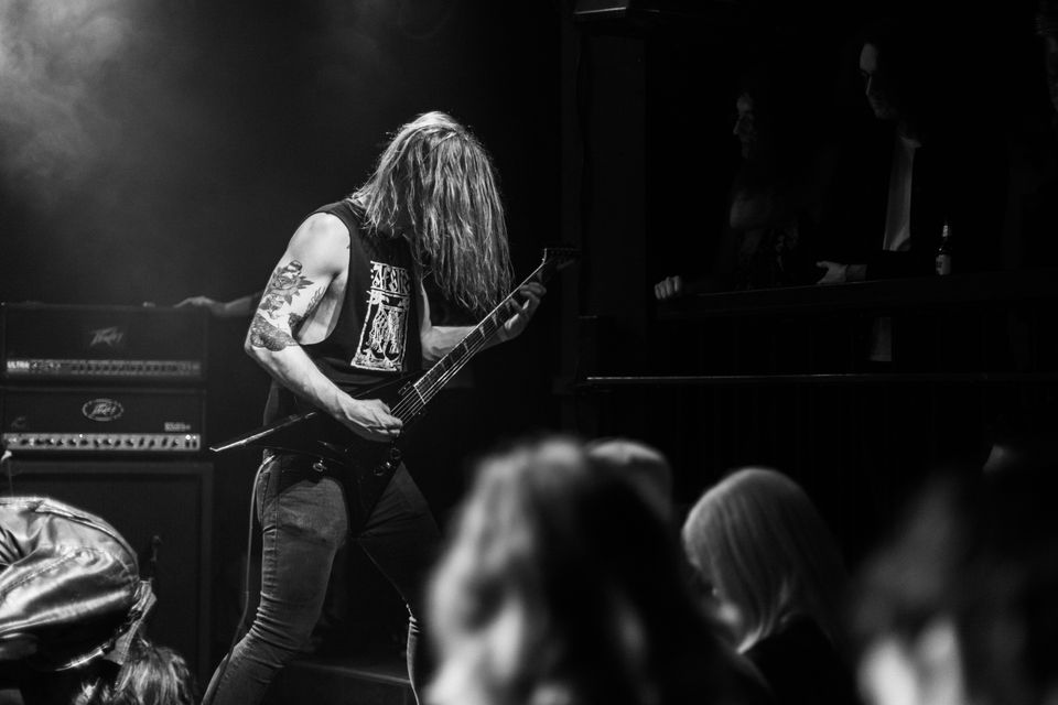 Ein metalmusikar stend på scena med røyk og lys og spelar intenst på elektrisk gitar.