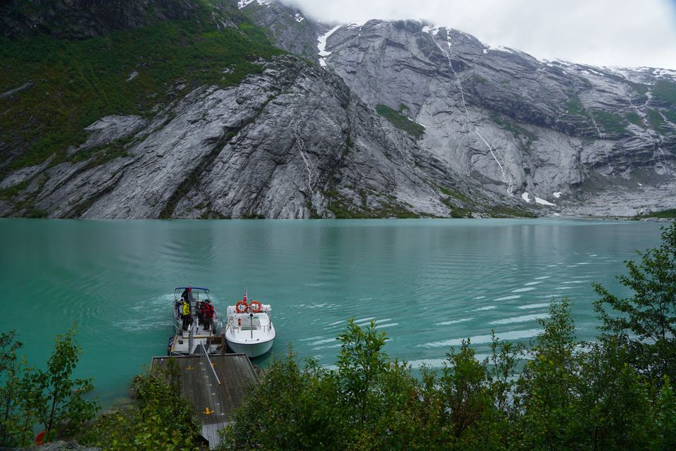 Ein gondol heng i lufti yver ein djup fjord, med bratte fjell og brear kring.